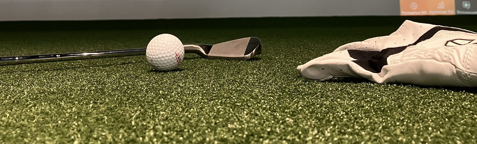 Piłka golfowa, iron i rękawica na macie symulatora Screen Golf