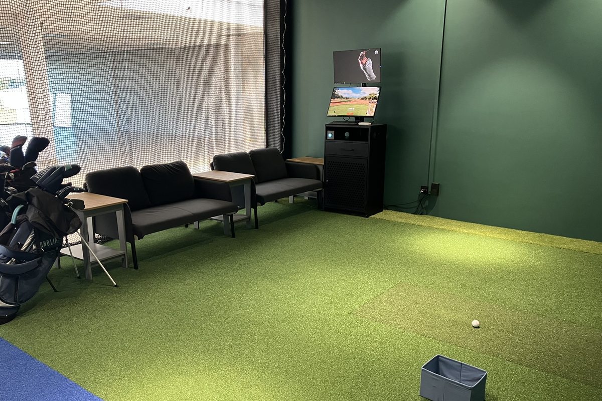 Strefa wypoczynkowa z kanapami i stolikami obok stanowiska symulatora golfowego
